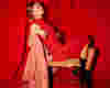 woman sat in a chair wearing a red dress and sat in front of a red back drop