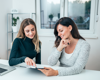 two woman sat at the desk working together