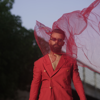 man in red suit posing with red fabric blowing in his face
