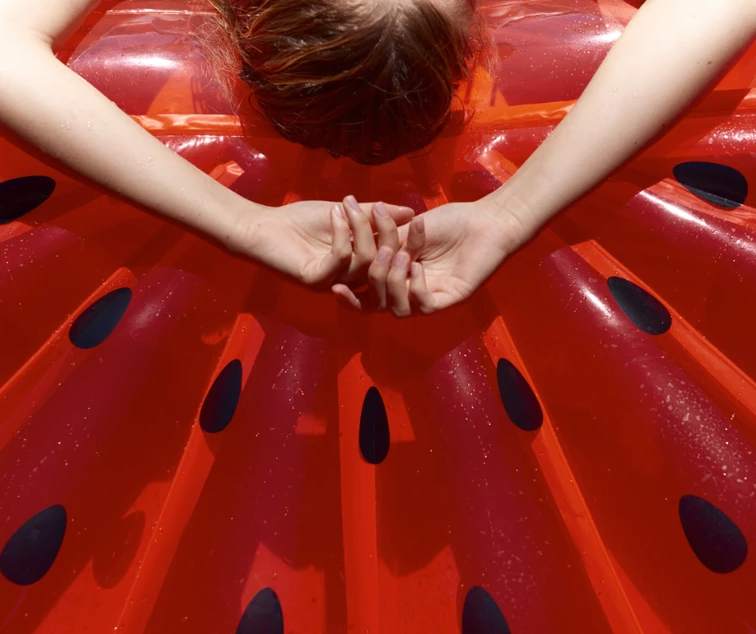 woman laying on inflatable red watermelon with hands above head