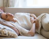 woman lying on the sofa holding her stomach in pain