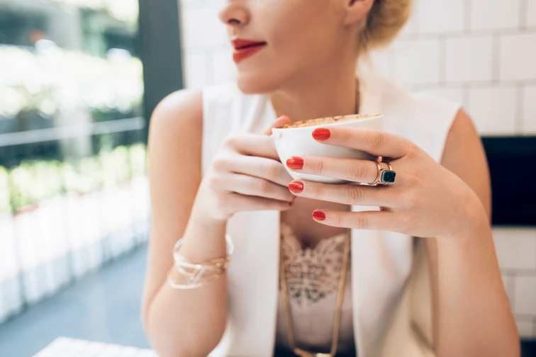 woman sat in a cafe looking out the window. The image is focused on her coffee cup and red nails