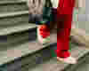 woman wearing red trousers, walking down a set of stairs holding a bag