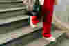 woman wearing red trousers, walking down a set of stairs holding a bag