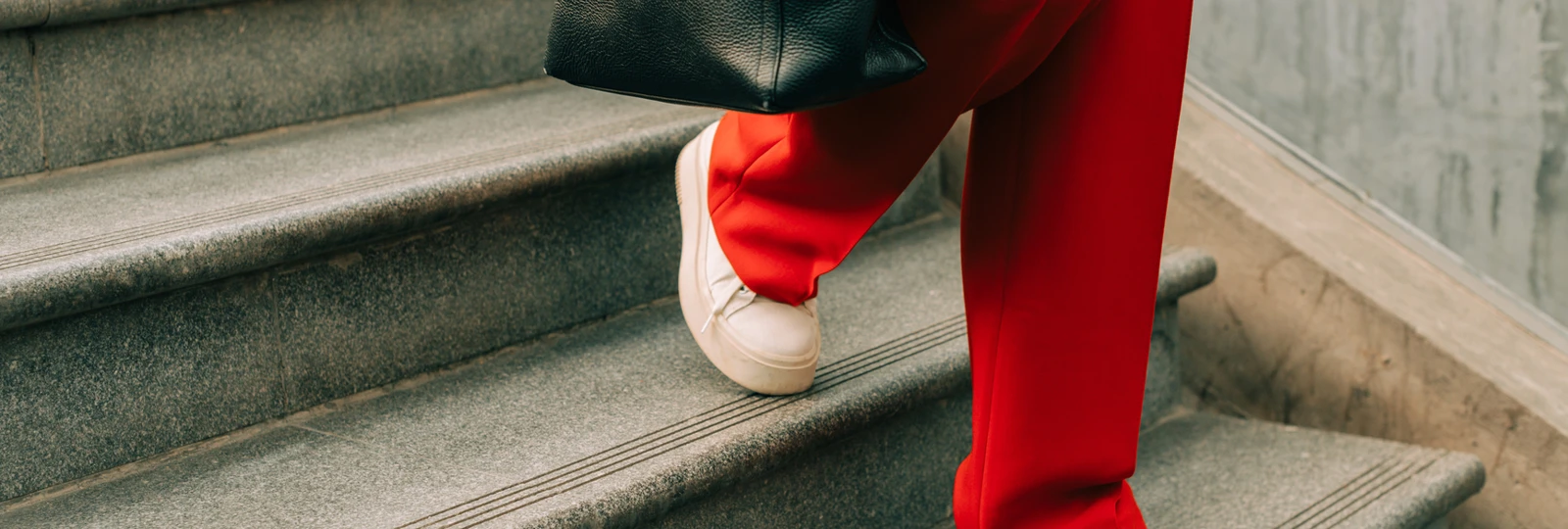 woman wearing red trousers, walking down a set of stairs holding a bag