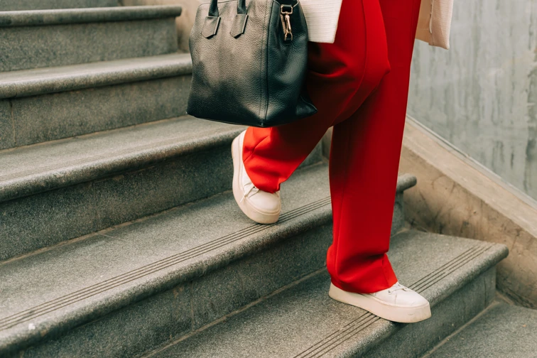 woman wearing red trousers, walking down a set of stairs holding a bag