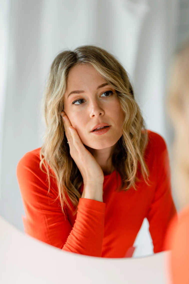 woman in red shirt staring into mirror