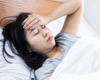 woman laying in bed holding hand up to forehead in pain