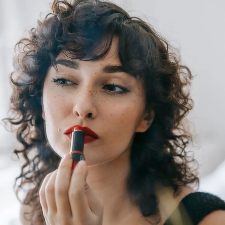 woman applying red lipstick in a mirror