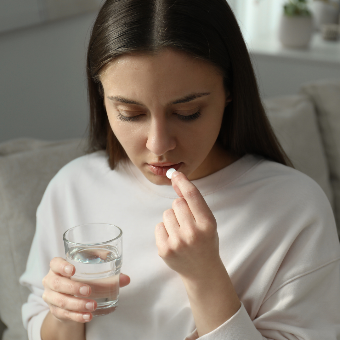 woman looking down taking tablet with glass of water 