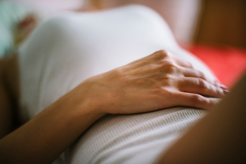 woman wearing a white vest, holding her stomach due to periods.