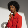 woman in red suit and finger on face looking into camera
